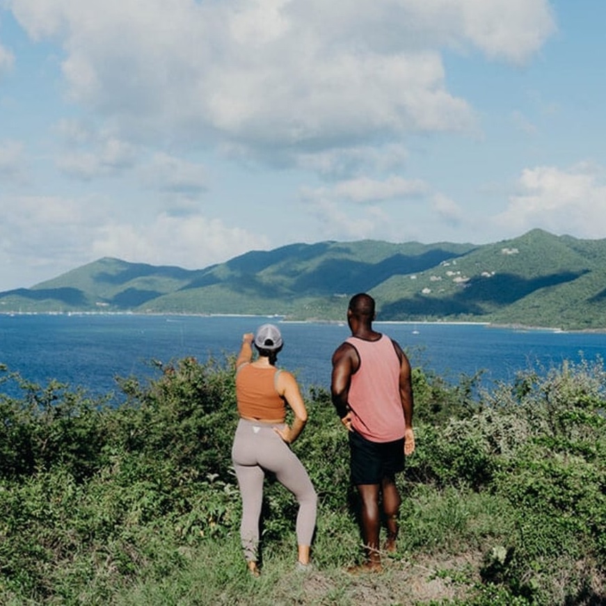 Two hikers overlooking the turquoise Caribbean Sea and lush green islands from a scenic hillside trail